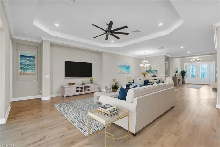 Living room featuring light hardwood / wood-style floors, ceiling fan with notable chandelier, ornamental molding, and a tray ceiling