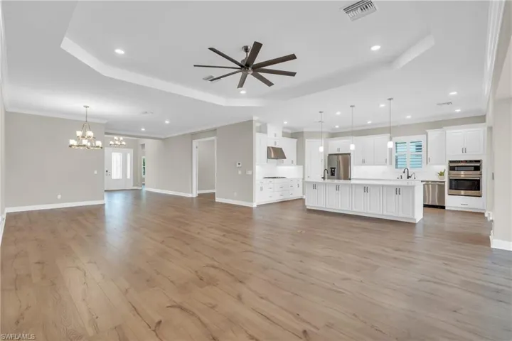 Unfurnished living room featuring ceiling fan with notable chandelier, sink, a raised ceiling, crown molding, and light hardwood / wood-style flooring