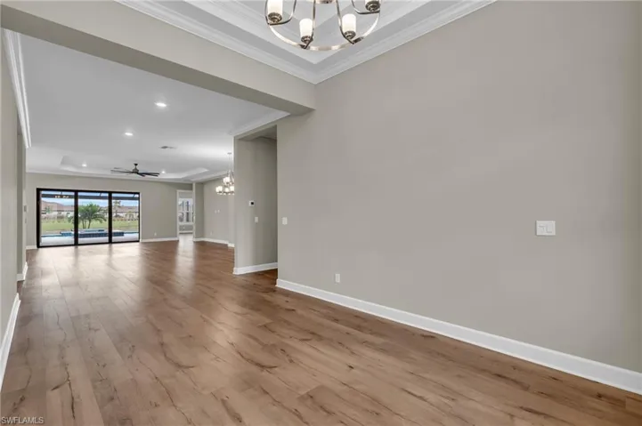 Unfurnished room with a tray ceiling, ceiling fan with notable chandelier, ornamental molding, and light hardwood / wood-style flooring
