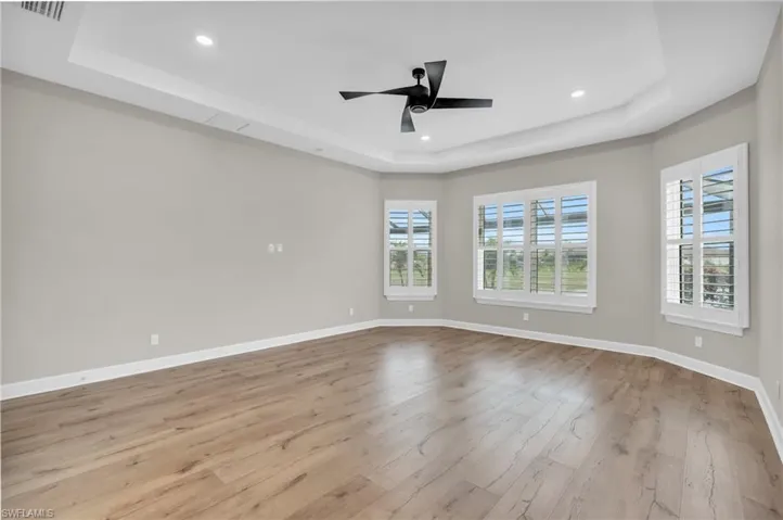 Empty room with light hardwood / wood-style floors, ceiling fan, and a raised ceiling