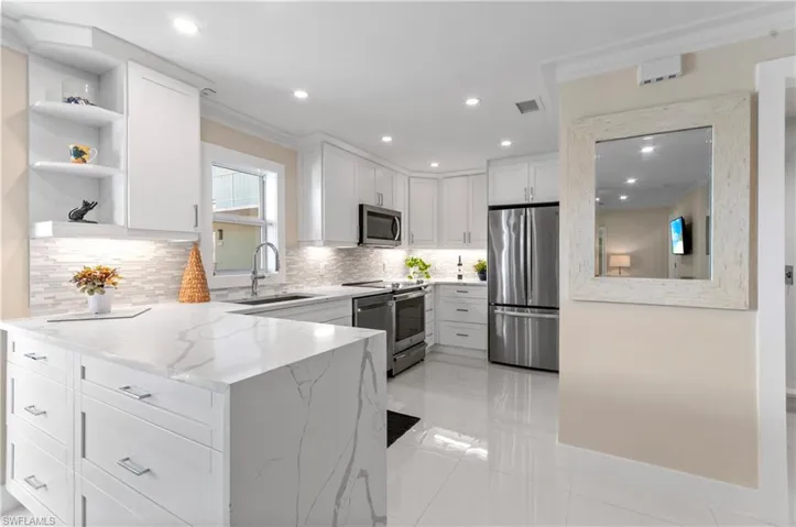 Kitchen featuring light stone countertops, crown molding, white cabinetry, appliances with stainless steel finishes, and a peninsula
