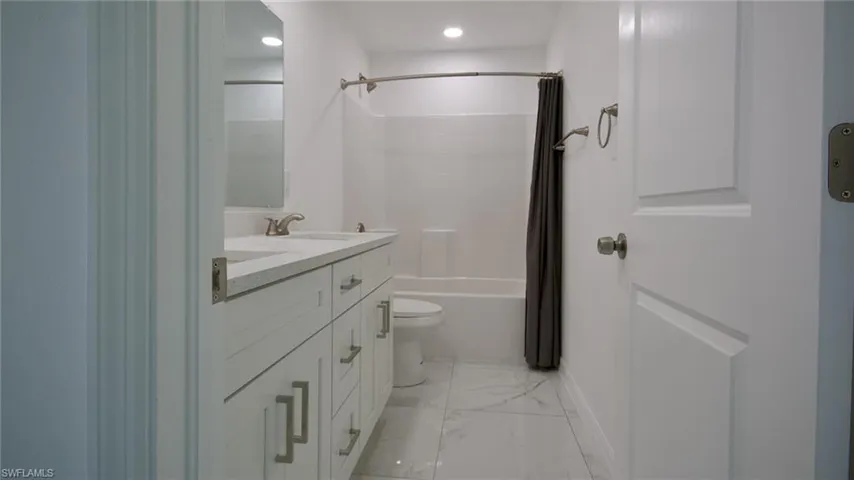 Full bath with marble finish floor, shower / tub combo, toilet, and double vanity