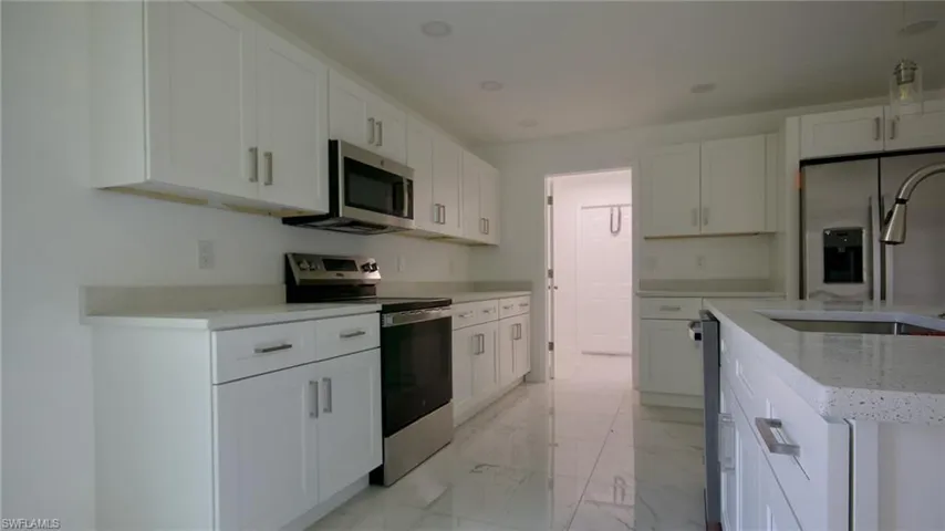 Kitchen featuring white cabinetry, stainless steel appliances, marble finish floor, a sink, and light stone countertops