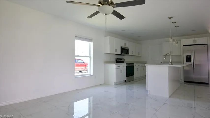 Kitchen with white cabinetry, stainless steel appliances, baseboards, marble finish floor, and a ceiling fan