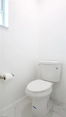 Bathroom with marble finish floor, baseboards, and toilet