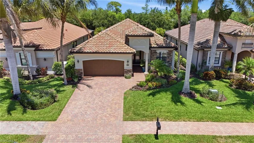 Mediterranean-style residence featuring a tile roof, an integrated garage with a wood-finish door, and a paver driveway