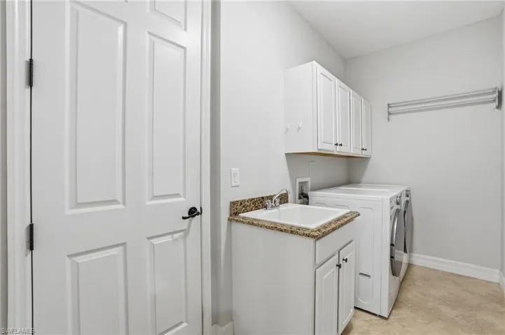 Functional utility room featuring a built-in sink with a granite-look countertop, white cabinetry with black hardware, and a wall-mounted drying rack