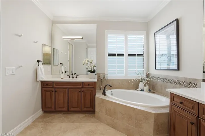 Bathroom featuring a built-in soaking tub with tiled surround, wood-finish vanity with countertop, and plantation shutters