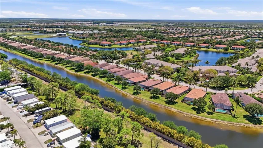 Aerial perspective showcasing a residential community with numerous homes featuring terracotta-style roofs, surrounded by lush green landscaping and mature palm trees