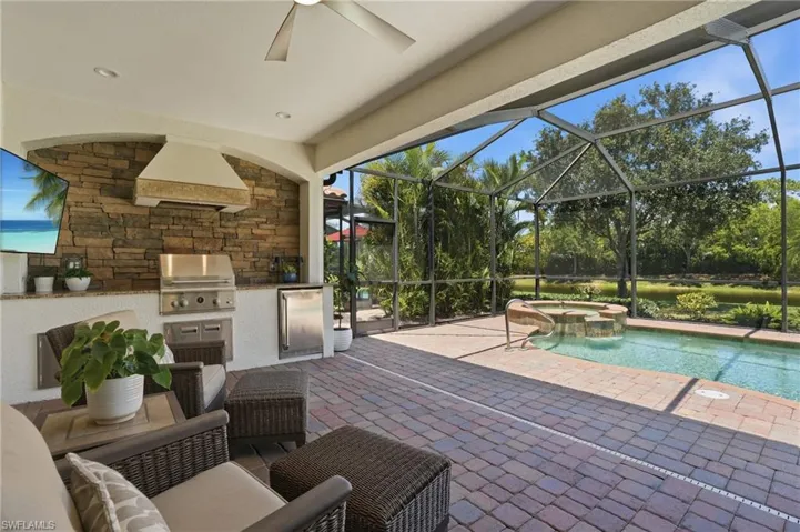 Screened outdoor living area featuring a built-in outdoor kitchen with a stone-accented wall, stainless steel grill, and refrigerator