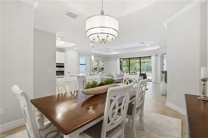 Open-concept dining area featuring a tray ceiling, recessed lighting, and a modern drum pendant light fixture