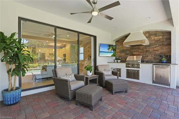 Covered outdoor living space featuring a built-in outdoor kitchen with stainless steel grill and refrigerator, stone-accented wall, and recessed lighting