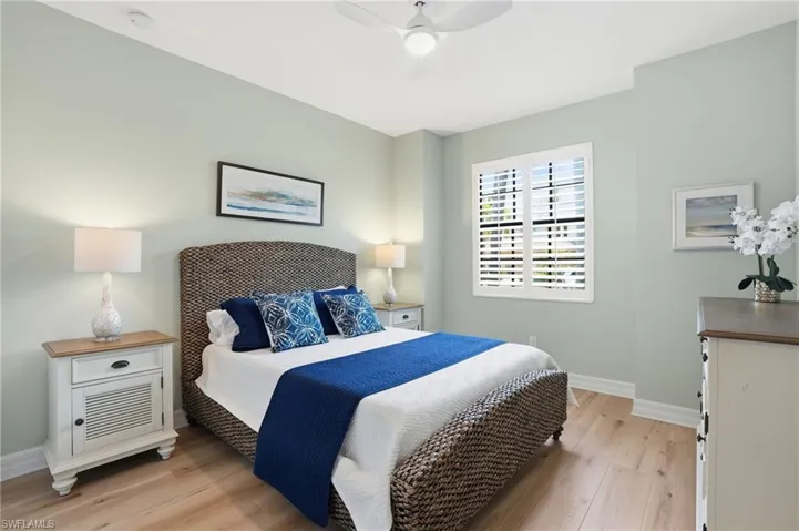 Bedroom featuring light wood-finish flooring, a ceiling fan with integrated lighting, and a window with plantation shutters