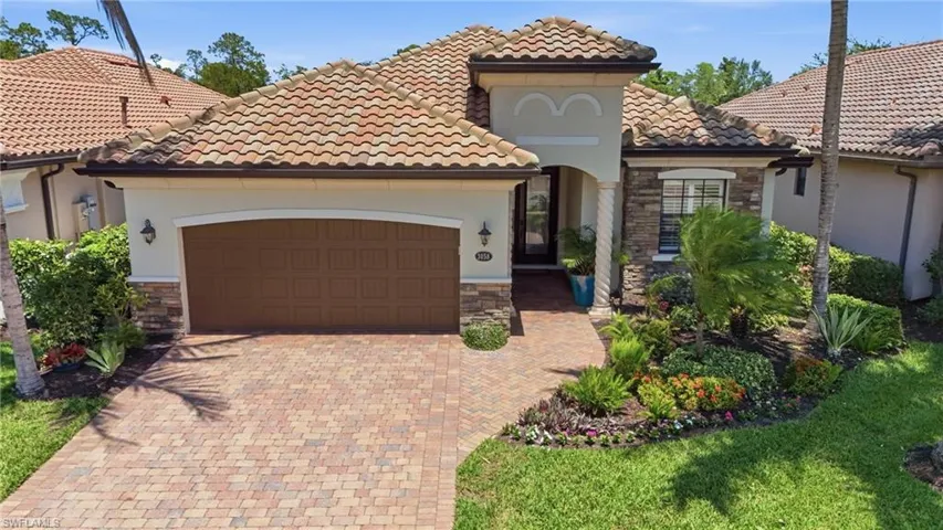 Mediterranean-inspired exterior featuring a barrel tile roof, stacked stone accents, a paver driveway, and an arched entry with a decorative column