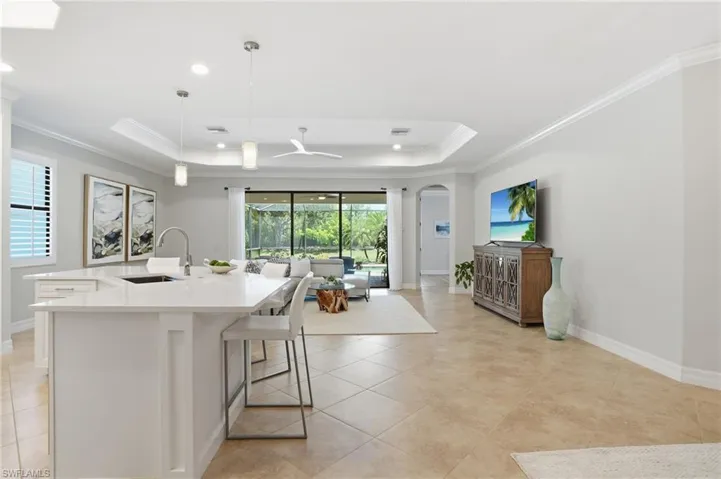 Open-concept living area featuring large format tile flooring, a kitchen island with integrated sink, pendant lighting, and a tray ceiling