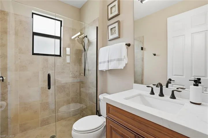 Bathroom featuring a glass-enclosed shower with tile surround, a built-in window, a vanity with a white countertop and integrated sink, and an oil-rubbed bronze faucet