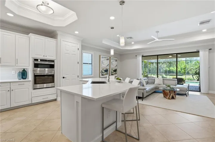 Open-concept living space featuring a central kitchen island with a white countertop, built-in stainless steel double ovens, and large sliding glass doors opening to the screened outdoor area