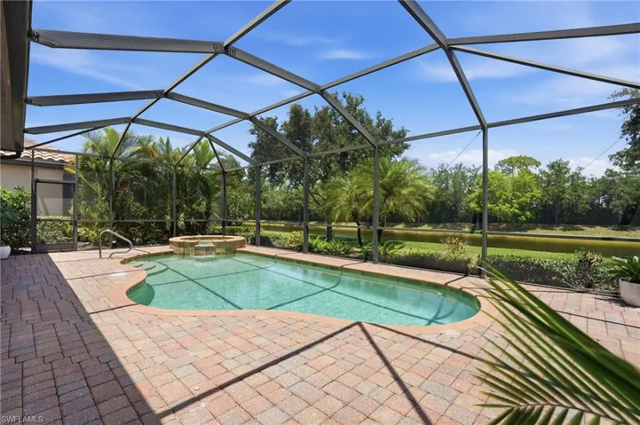 Screened outdoor living area featuring a freeform swimming pool, integrated spa with waterfall, paver deck, and tropical landscaping