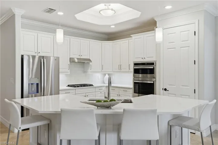 Spacious kitchen featuring an angular island with integrated sink, white cabinetry, stainless steel appliances, a tile backsplash, and recessed lighting