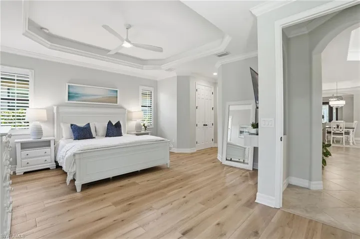 Spacious room featuring wood-finish flooring, a tray ceiling with crown molding, and plantation shutters