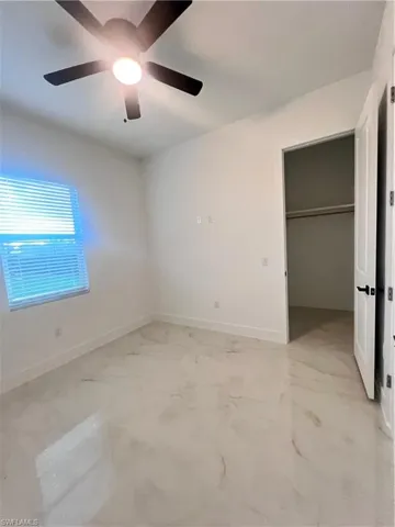 Unfurnished bedroom with a ceiling fan, light marble finish flooring, and a closet