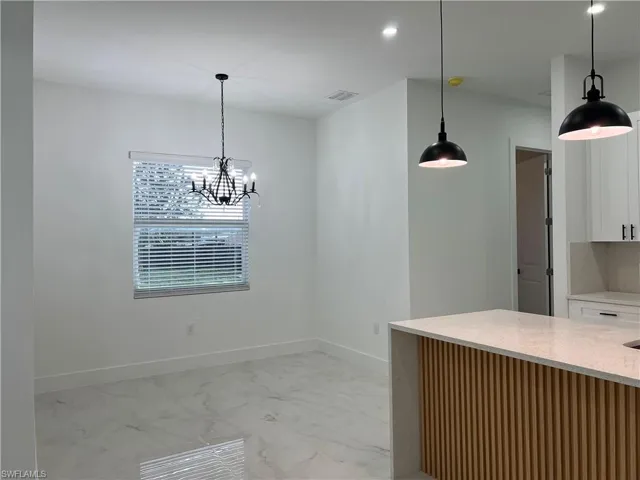 Kitchen featuring light marble finish floors, white cabinets, and pendant lighting