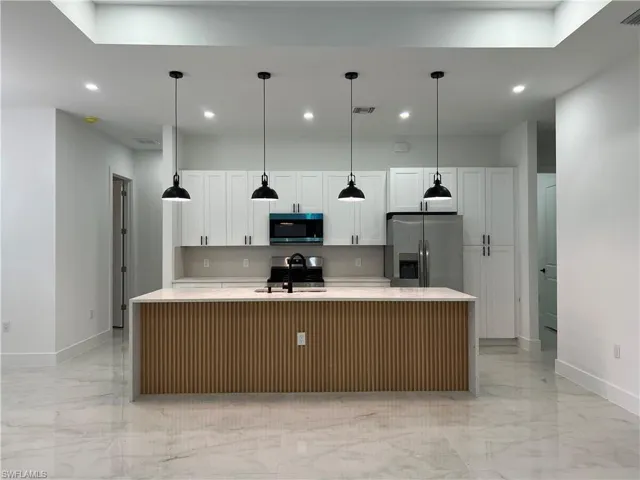 Kitchen featuring stainless steel appliances, light marble finish flooring, recessed lighting, an island with sink, and white cabinets