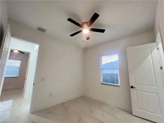 Unfurnished bedroom featuring light marble finish floors and a ceiling fan