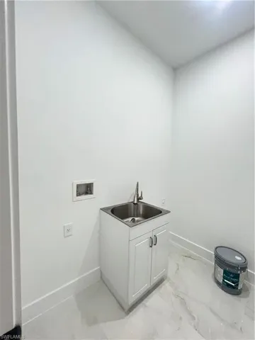 Laundry area featuring hookup for a washing machine, light marble finish floors, and cabinet space