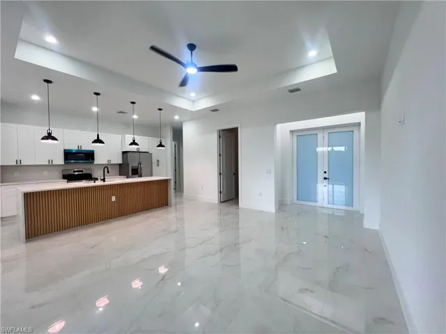 Kitchen featuring stainless steel appliances, a ceiling fan, a tray ceiling, open floor plan, and light countertops