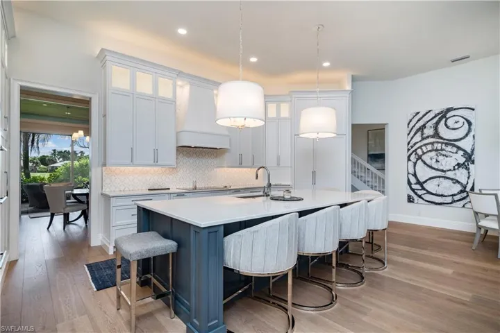 Kitchen featuring a kitchen island with sink, pendant lighting, light hardwood / wood-style flooring, custom range hood, and white cabinets floors, and custom range hood