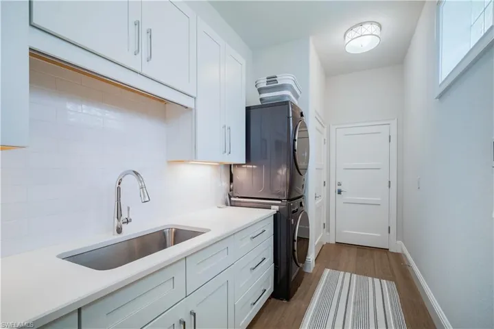 Laundry room w/ white cabinetry, tasteful backsplash, stacked washer/dryer and laundry sink