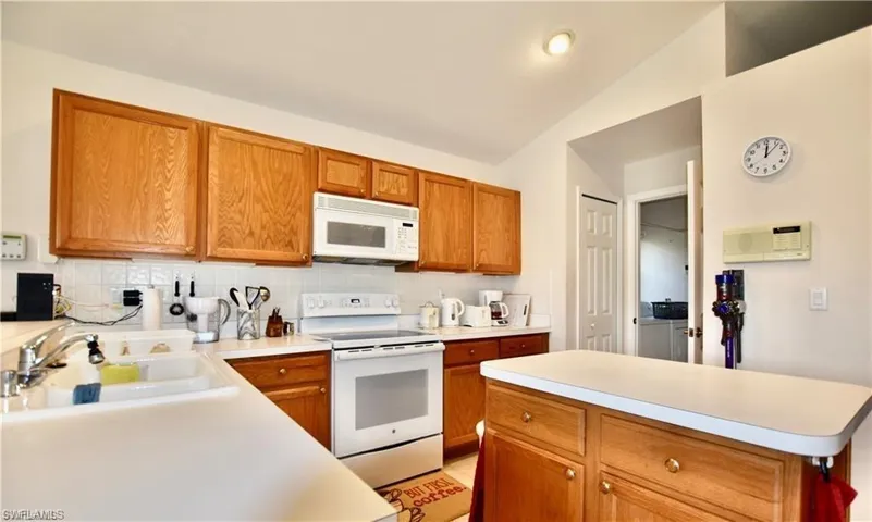 Kitchen with decorative backsplash, white appliances, sink, lofted ceiling, and independent washer and dryer