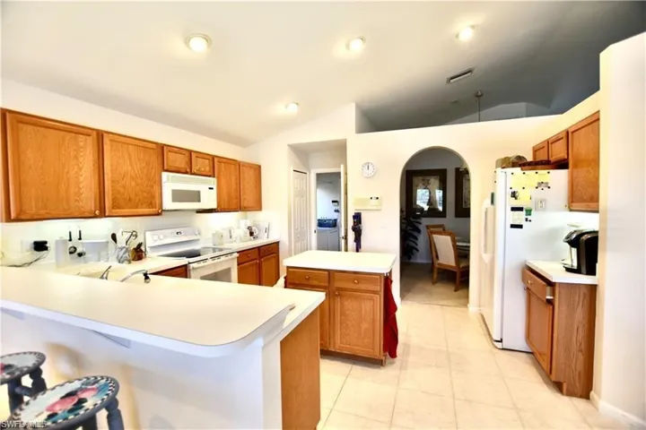 Kitchen featuring kitchen peninsula, light tile patterned floors, vaulted ceiling, and white appliances