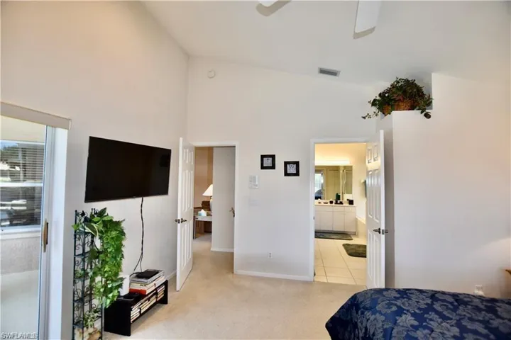 Bedroom with ensuite bathroom, ceiling fan, lofted ceiling, and light colored carpet