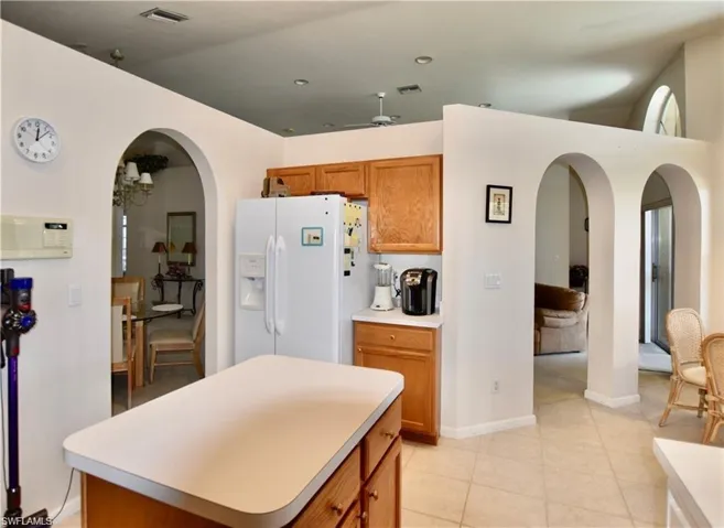 Kitchen with a kitchen island, white refrigerator with ice dispenser, ceiling fan, and light tile patterned floors