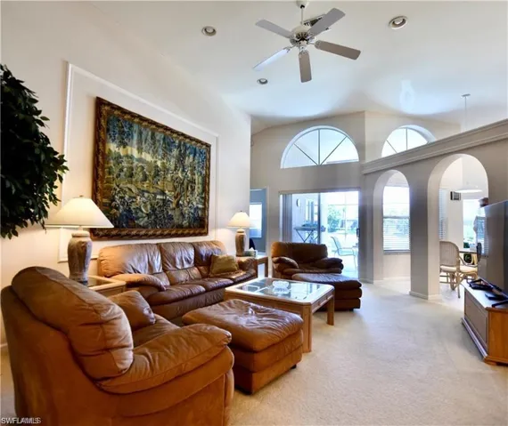 Carpeted living room with high vaulted ceiling and ceiling fan