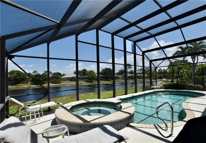 View of pool featuring an in ground hot tub, glass enclosure, a water view, and a patio area