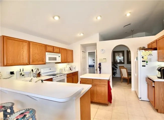 Kitchen with white appliances, kitchen peninsula, lofted ceiling, light tile patterned flooring, and a center island