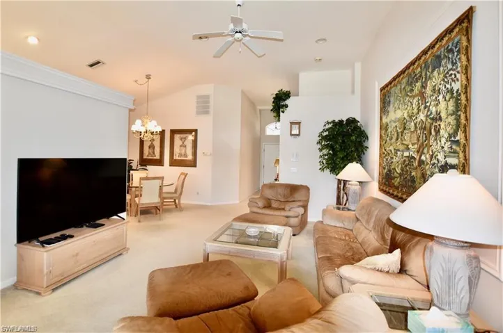 Living room with lofted ceiling, light carpet, and ceiling fan with notable chandelier