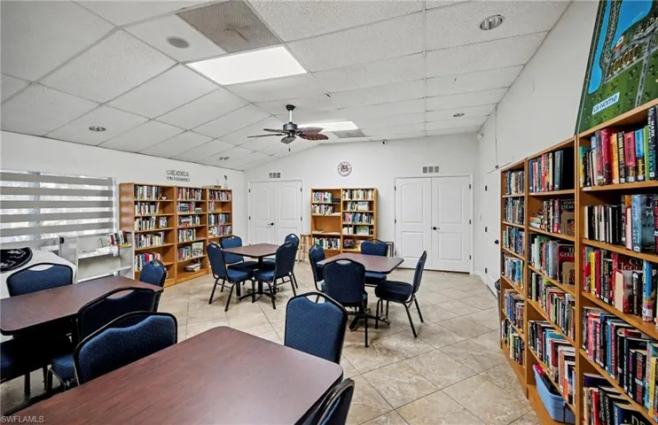 Library area featuring bookshelves, a drop ceiling, vaulted ceiling, and ceiling fan