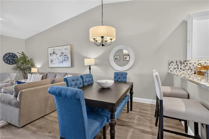 Vaulted ceiling with a drum pendant light fixture, wood-finish flooring, and a kitchen pass-through with granite countertops and a mosaic tile backsplash
