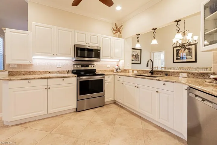 Kitchen with appliances with stainless steel finishes, white cabinets, decorative backsplash, ceiling fan with notable chandelier, and ornamental molding