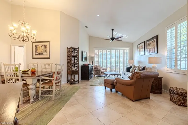 Living room with ceiling fan with notable chandelier, vaulted ceiling, light tile patterned floors, and plenty of natural light