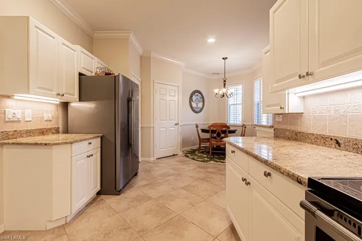 Kitchen featuring high end fridge, tasteful backsplash, light stone counters, hanging light fixtures, and crown molding