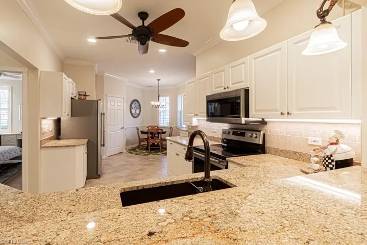 Kitchen with ceiling fan with notable chandelier, hanging light fixtures, stainless steel appliances, and backsplash