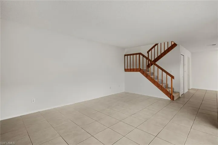 Spacious room featuring neutral tile flooring and a carpeted staircase with wood-finish railings