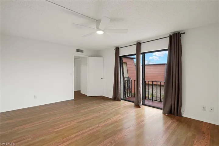 Bright room featuring wood-finish flooring, a white ceiling fan with integrated lighting, and a private balcony accessed through sliding glass doors