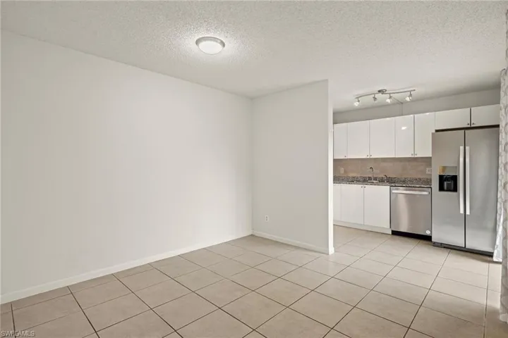 Neutral-toned tile flooring extends into a kitchen featuring white flat-panel cabinetry, stainless steel appliances, and track lighting