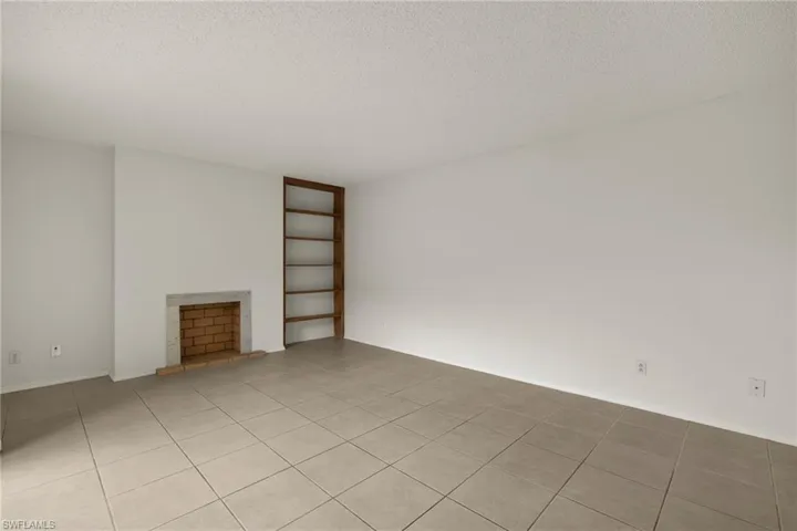 Living area featuring a brick fireplace with a stone hearth, built-in wooden shelving, and square tile flooring